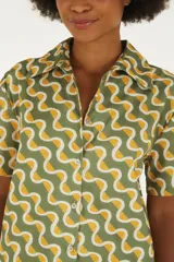 Vestido corto de algodón con estampado geométrico de ondas en tonos verde, amarillo y blanco, con cuello camisero, manga corta y cierre frontal de botones.