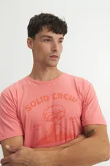 Remera de algodón color coral con cuello redondo, mangas cortas y estampa frontal con el texto 'SOLID CREW' y un diseño gráfico de un volcán en tonos naranja.