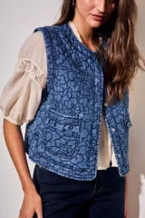 Chaleco capitoneado de jean azul con bordados florales en tono oscuro, cuello redondo y bolsillos delanteros aplicados con solapa fruncida.