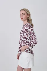 Camisa de viscosa con estampado botánico en tonos bordó sobre fondo blanco, cuello mao y cierre frontal con botones. Presenta bolsillos frontales y mangas tres cuartos.