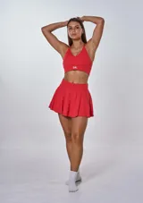 Conjunto deportivo compuesto por un top con escote en V y espalda deportiva, y una pollera short con diseño plisado. El top presenta el logo de la marca estampado en el frente.