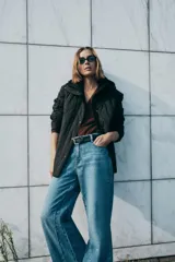 Chaqueta acolchada de color negro con diseño de costuras onduladas, cuello subido y capucha ajustable. Cuenta con cierre frontal de cremallera oculto por una solapa con botones a presión, mangas largas y bolsillos laterales. Tejido con tecnología repelente al agua.