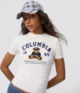 Remera de algodón con elastano, color blanco, de corte ajustado al cuerpo y manga corta. Cuenta con cuello redondo y estampa frontal estilo college con un oso sentado, la inscripción "Columbia", el número 1989 y la frase "Calm and Cute Bears".