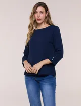 Buzo liviano de corte recto en color azul marino, confeccionado en tela texturizada en relieve. Presenta escote bote, mangas 3/4 con puños anchos decorados con tres botones y bolsillos laterales funcionales integrados mediante costuras verticales.