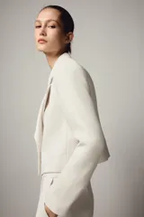 Blazer corto de cuello solapa y manga larga con hombreras. Presenta un diseño cruzado con cierre frontal de dos botones dorados.