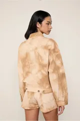 Chaqueta de algodón con estampado tie-dye en tonos beige y marrón claro, de corte recto, con cuello clásico, cierre frontal con cremallera, mangas largas y bolsillos frontales.