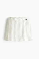Short pollera mini de corte cruzado con diseño a rayas verticales. Presenta un botón decorativo en la parte frontal y cierre lateral oculto.
