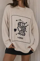 Sweater de punto color crudo con cuello redondo y diseño holgado, con un parche frontal bordado a mano en negro que representa el signo zodiacal de Virgo.