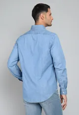Camisa de jean azul con botones blancos, mangas largas con puños doblados y corte clásico.