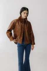 Camisa marrón de cuero sintético con cuello de piel sintética color marrón, cierre frontal con botones a presión dorados, dos bolsillos con solapa en el pecho y corte holgado.