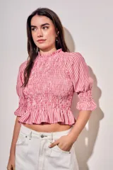 Blusa de algodón con diseño a rayas verticales en tonos rosa y blanco. Presenta un cuerpo con fruncido elástico (smock), cuello alto con volados y mangas tres cuartos abullonadas con terminación en volado.