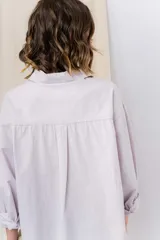 Camisa verde pastel de algodón, corte oversize, con cuello camisero, cierre con botones, mangas largas con puños con volados de encaje blanco, dos bolsillos frontales con solapa y ruedo irregular. 