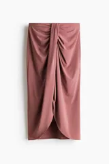 Pollera midi de punto suave, color rosado, con cintura elástica de tiro alto y detalle girado adelante para crear un efecto drapeado, con bajo asimétrico y abertura frontal.