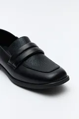 Mocasín negro de cuero sintético con punta cuadrada, detalle de textura en la capellada y taco bajo de 2,5 cm.