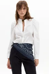 Camisa blanca de popelina de algodón con cuello mao, cierre frontal con botones de nácar y mangas largas con hombros fruncidos y puños rectos.