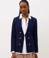Blazer cruzado de sastrería en color azul marino, con corte slim y estructura entallada. Presenta solapas de muesca, cierre frontal con seis botones dorados metálicos con relieve, bolsillos con solapa en los laterales y mangas largas.