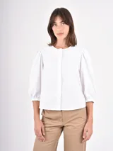 Camisa blanca de corte clásico con cuello redondo y cierre frontal oculto. Presenta mangas tres cuartos abullonadas con puños elásticos, brindando un toque femenino y moderno.