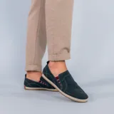 Alpargata de gamuza color verde oscuro, con detalle de elástico lateral a rayas rojas y blancas. Presenta una suela con borde de yute trenzado y base de goma.