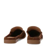 Zuecos de gamuza marrón estilo mocasín, abiertos en el talón con diseño slip-on. Presentan costuras pespunteadas visibles, detalle de tira sobre el empeine con un aplique metálico dorado y suela plana.