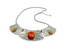 Collar llamativo de placas articuladas en metal plateado con acabado texturizado martillado, adornado con una piedra central de tono anaranjado y dos piedras laterales de tono marfil, con cadena de estilo cola de ratón y extensor.