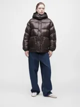 Campera puffer de corte holgado en color marrón oscuro con acabado brillante. Presenta cuello alto, cierre frontal con cremallera y botones a presión, además de bolsillos frontales con solapa.