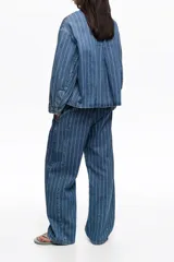 Chaqueta corta de denim en color azul con diseño de rayas verticales blancas, cuello camisero, bolsillos delanteros de parche y cierre frontal con botones metálicos.