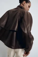 Chaqueta bomber de piel color marrón oscuro, con cuello alto, cierre frontal con cremallera y solapa con botones ocultos. Presenta mangas largas, bolsillos delanteros y un diseño de corte recto.