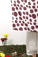 Pañuelo cuadrado de seda con estampado de lunares bordó sobre fondo beige y una gran ilustración central de una flor en tonos amarillos y marrones.