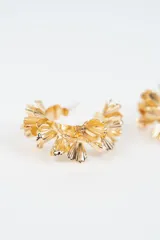 Aros tipo argolla dorados con diseño de pétalos metálicos superpuestos a lo largo de la estructura circular.