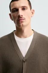 Cárdigan de hombre color negro, de corte regular fit, tejido en estructura compacta, con cuello pico, manga larga y cierre frontal de botonadura.