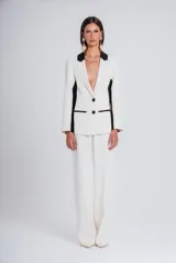 Blazer de corte sastrero en color marfil con detalles en negro en solapas, laterales y bolsillos. Presenta cierre frontal con dos botones y diseño estructurado.