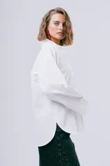 Camisa blanca de manga larga con cuello camisero, cierre frontal con botones y puños anchos.