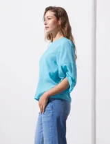 Blusa de gasa con estampado geométrico en tonos negro, gris y celeste. Tiene cuello redondo y mangas 3/4 amplias con abertura y botón.