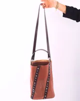 Matera tipo bucket de cuero color bordó, con detalles de tiras verticales en cuero negro adornadas con remaches metálicos plateados. Cuenta con un asa de mano fija y un compartimento interior amplio.