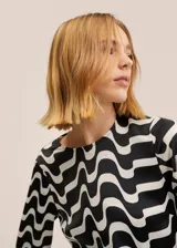 Vestido corto de manga larga con cuello redondo, confeccionado en tela satinada con estampado geométrico de ondas en blanco y negro.