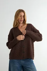 Cardigan de punto con diseño de trenzas, color marrón, escote en V y cierre frontal con botones oscuros. Presenta mangas largas con puños ajustados y un corte holgado.