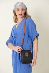 Cartera bandolera de cuero negro con textura granulada, detalle de solapa frontal en color tostado con cierre de botón a presión y correa larga ajustable en color tostado.