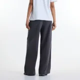 Pantalón de jogging New Balance modelo Trackside, color gris oscuro, de corte holgado y pernera ancha. Confeccionado en felpa francesa suave, cuenta con cintura elástica ajustable con cordón y un pequeño estampado y bordado en la pierna izquierda.