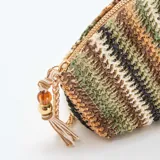 Bolso tipo clutch con diseño en forma de saco, tejido a rayas diagonales en tonos verdes, marrones y beige. Cuenta con cierre superior de cremallera, correa de cadena dorada y detalle colgante de borla con cuentas.