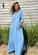 Vestido camisero largo de jean, con cierre frontal de botones, cuello camisero, mangas largas y detalle de volado en el ruedo.