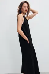 Vestido midi de color marrón con acabado satinado, cuello redondo con detalle fruncido y diseño sin mangas. Presenta un corte fluido con bajo asimétrico y bolsillos laterales ocultos.