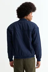 Campera tipo bomber color tostado, con cierre frontal, cuello, puños y ruedo de tejido elástico acanalado. Presenta costuras horizontales en la parte superior del pecho.