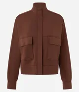 Campera de corte recto y largo, color marrón chocolate, con cuello alto, cierre frontal completo y bolsillos frontales tipo cargo con solapa. Presenta puños y ruedo acanalados.