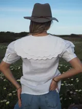 Blusa blanca de lino, de manga corta, con cuello marinero amplio decorado con estampado azul.