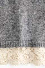 Buzo de punto holgado con mezcla de lana y mohair, color gris. Presenta cuello alto, hombros caídos y mangas largas. El bajo está decorado con un ribete de encaje en color crema en contraste.