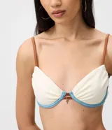 Top de bikini de media copa con aro, confeccionado en microfibra texturizada color blanco con detalles en celeste y tirantes finos marrones. Cuenta con un pequeño aplique metálico decorativo en el centro.