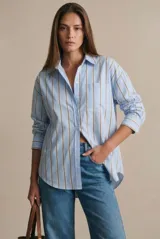 Camisa de corte oversize con estampado de rayas verticales en tonos azul claro y mostaza. Presenta cuello clásico, cierre frontal con botones y mangas largas con puños abotonados.