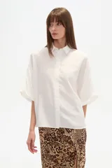 Camisa de viscosa color blanco, de corte holgado, con cuello clásico y cierre frontal de botones. Presenta mangas cortas con diseño amplio.