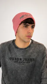 Gorro tipo beanie de punto acanalado en color rosado, con bordado en hilo verde en la parte frontal.
