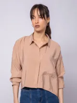 Camisa corta color beige de manga larga con botones nacarados y doble cartera. Cuenta con un bolsillo delantero y abertura trasera.